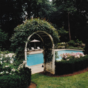 This rose covered arbor creates an inviting entranceway into a colorful landscaped pool garden.