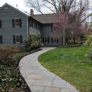 The colors in this long curving patterned bluestone walk complements the home.