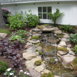 This natural stone pondless waterfall with stream enhances the beauty of the woodland garden.