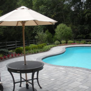 This pool patio design using pavers allows for a large seating area while enhancing the shape of the pool.